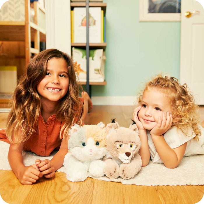 Sisters smiling and laying down with Soft Warm Weighted Bobcat Plush Warmies