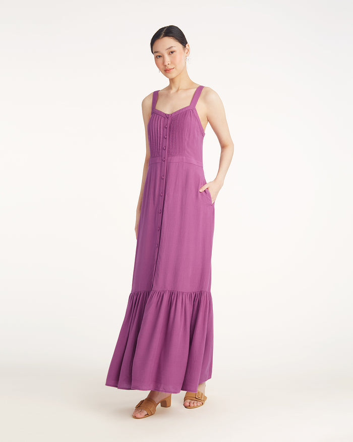 A woman wears the Draper James Brynn Sleeveless Midi Dress in Amethyst, featuring a button-down front and ruffled hem, paired with beige sandals, set against a plain white background.