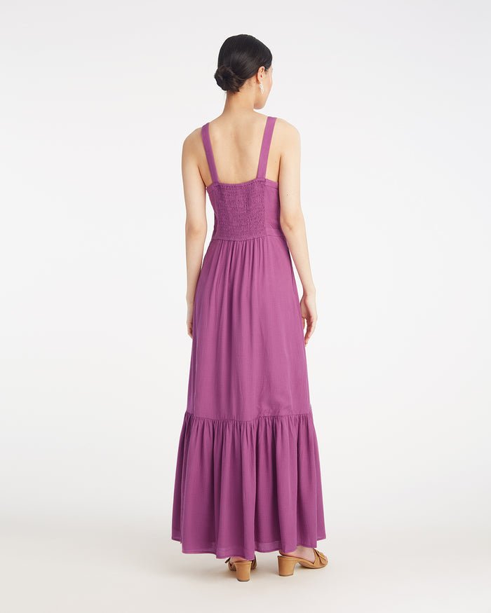 A woman faces away, wearing the Draper James Brynn Sleeveless Midi Dress in Amethyst—a fitted purple dress with a flared skirt—paired with tan sandals.