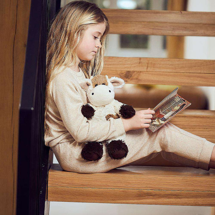 Little girl reading a book with Cute Weighted Lavender Scented Cow Stuffed Animal Heating Pad Warmies