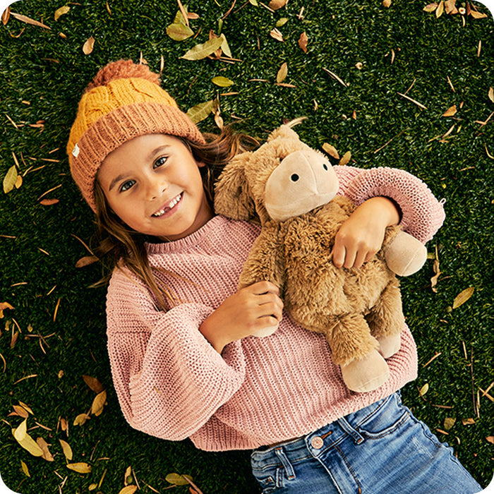 girl wearing sweater holding warmies donkey stuffed animal