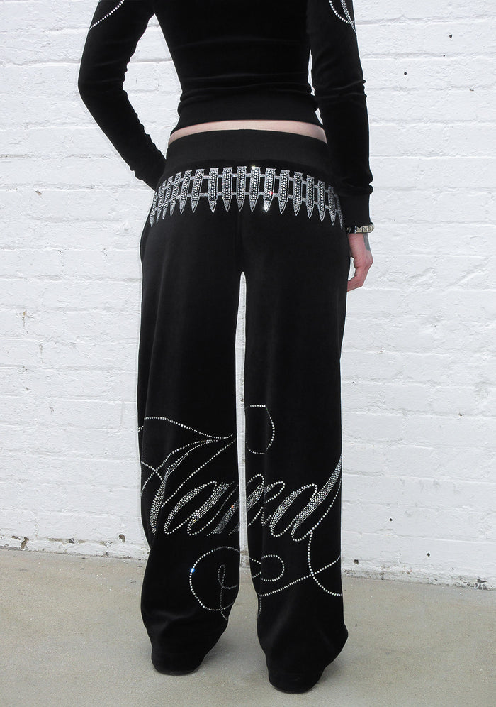 Model wearing black velour sweatpants with rhinestone embellishments, showcasing the back detail.