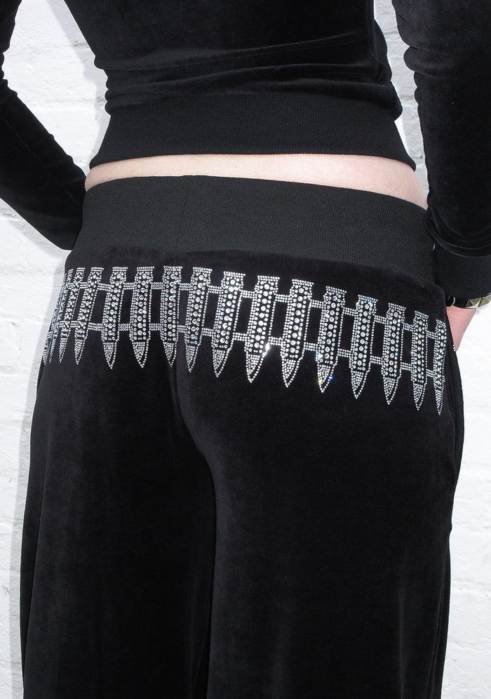 Back view of black velour sweatpants featuring rhinestone bullets design on the waistband.