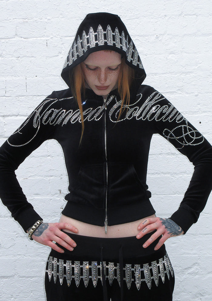 Model wearing a black hoodie with a rhinestone bullet design and zip closure, featuring logo embellishment.
