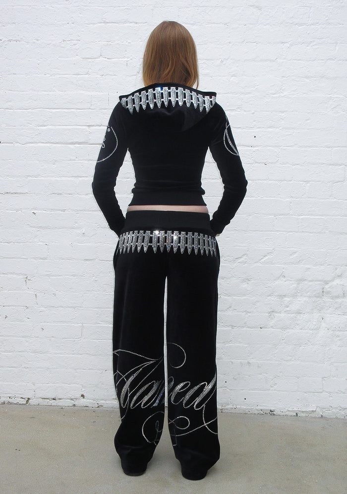 Model wearing a black hoodie with rhinestone bullet design and matching black pants, back view.