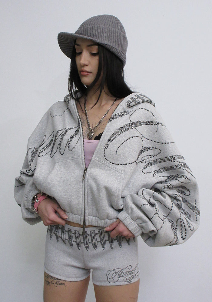 Model wearing the enemy studded crop zip hoodie grey marl with large studded details, front view.
