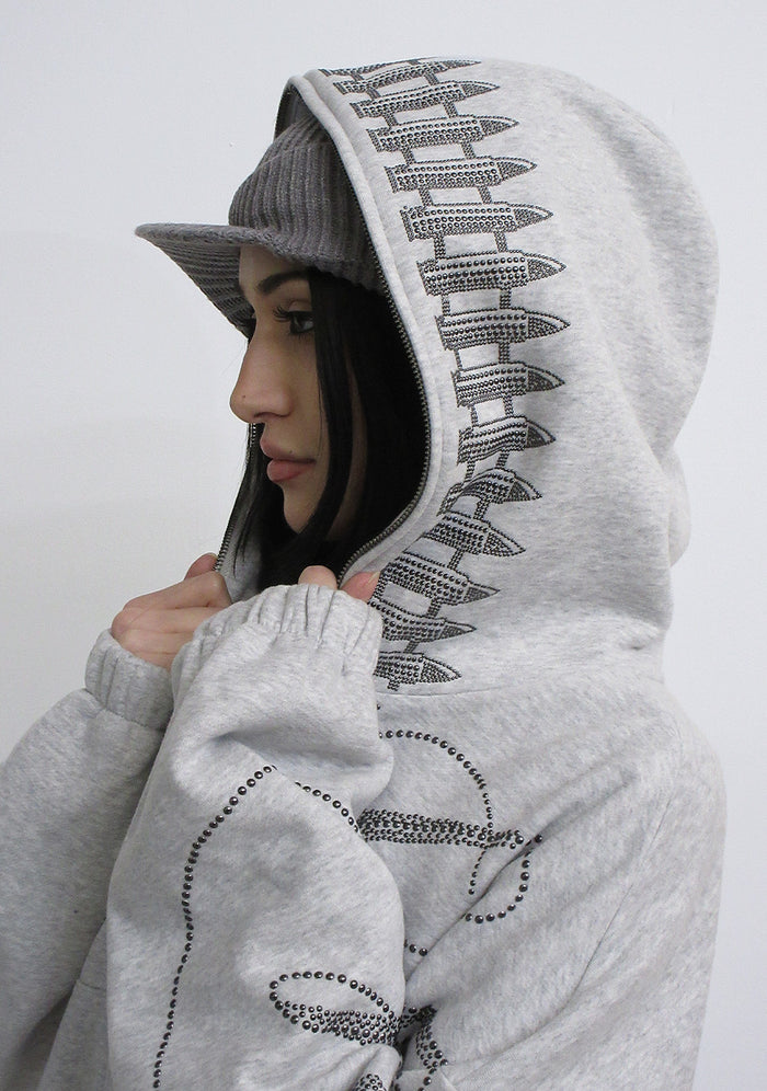 Side view of a model wearing the enemy studded crop zip hoodie grey marl featuring studded bullet details on the hood.