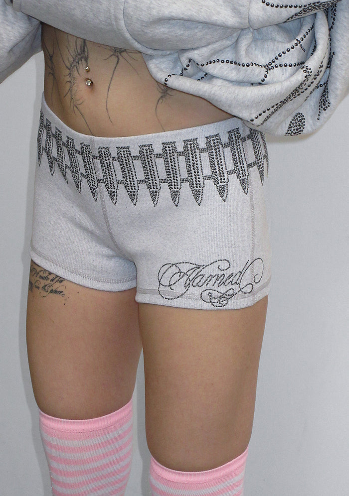 Model wearing grey marl hotpant shorts with studded logo design on the waistband.