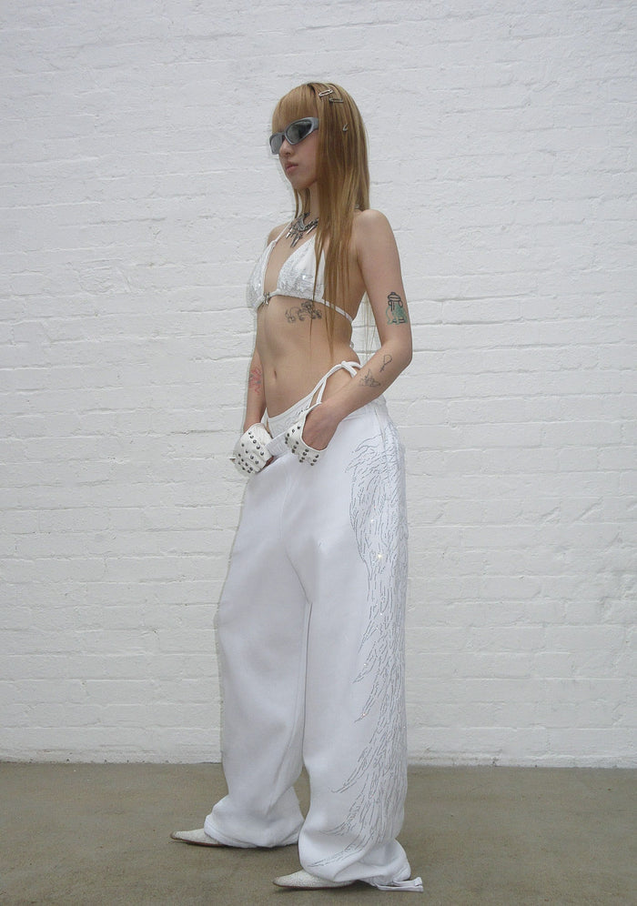 Model wearing fallen rhinestone oversized sweatpants white, featuring rhinestone wing design, in side view.