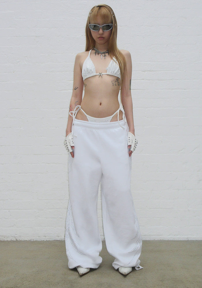 Model wearing fallen rhinestone oversized sweatpants white, showing adjustable ankle ties and rhinestone details.