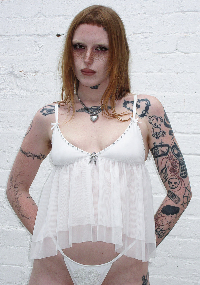 Model wearing a white cami top featuring rhinestones and sheer mesh details, with adjustable straps.
