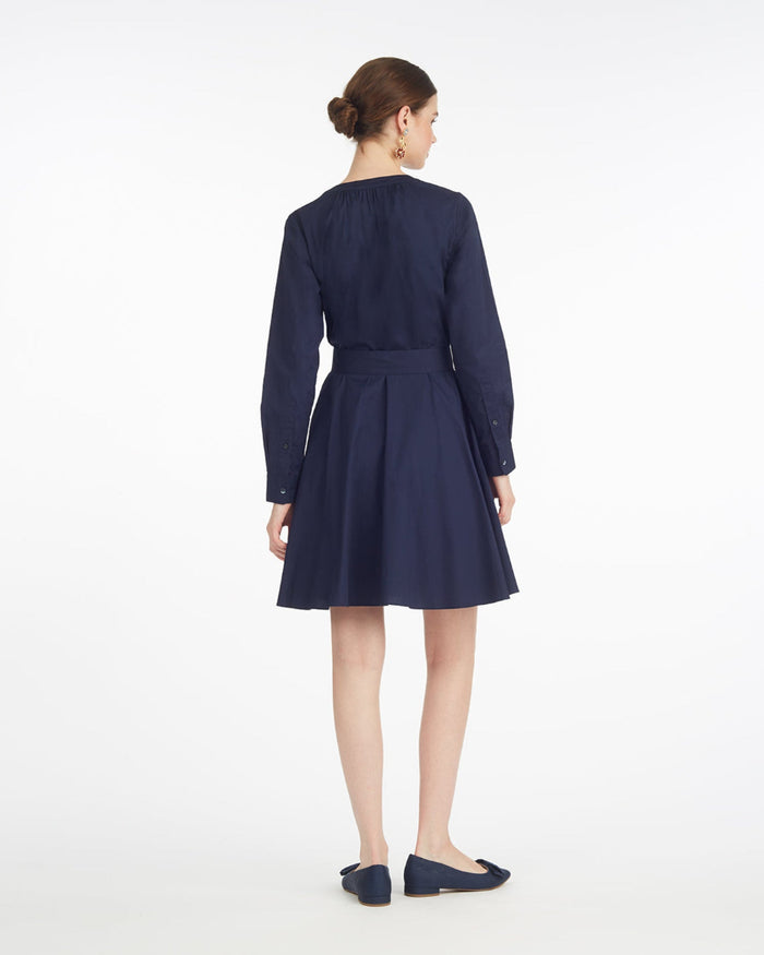 A woman stands facing away, wearing the Draper James Imogen Mini Shirtdress in navy cotton with a belted waist and matching navy flats, set against a plain white background.