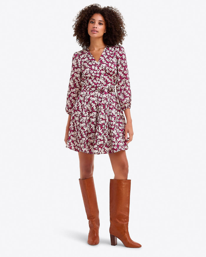 A woman wears the Draper James Jordan Long-Sleeve Wrap Dress in hammered satin with brown knee-high boots, standing against a plain white background.