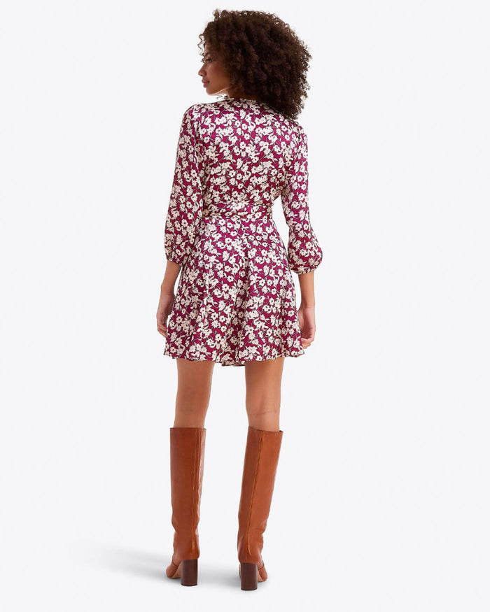 A woman stands with her back to the camera, wearing the Draper James Jordan Long-Sleeve Wrap Dress in hammered satin and brown knee-high boots.