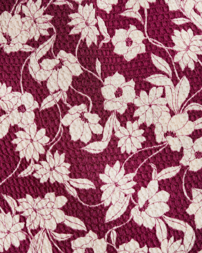 The Jordan Long-Sleeve Wrap Dress in Hammered Satin by Draper James features a maroon background with an off-white floral pattern of large flowers and leaves, offering a refined, textured look perfect for elegant occasions.