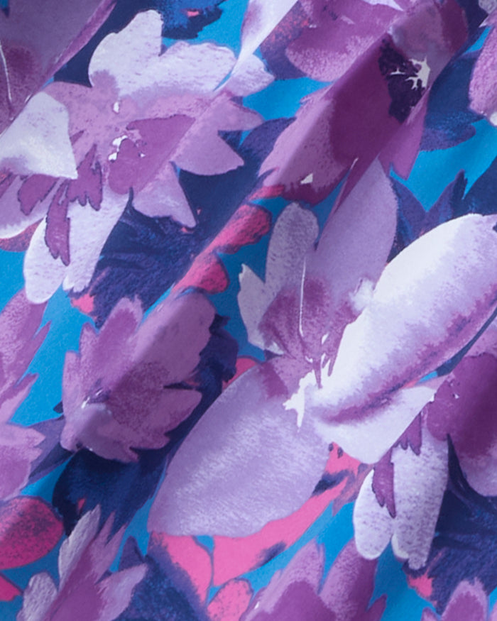A close-up of a bold floral fabric pattern with abstract purple and pink flowers on a deep blue background, similar to the elegant design on Draper James's Katie Midi Dress.