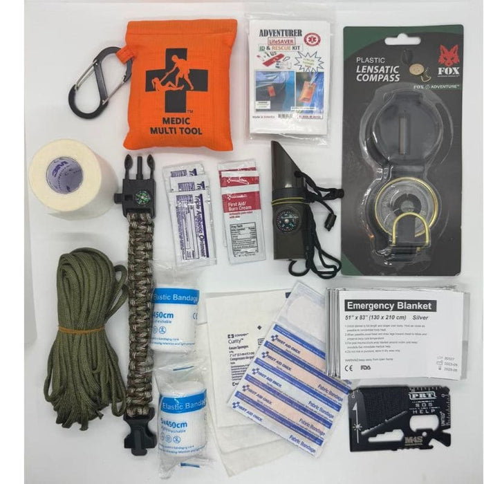 Collection of outdoor survival items including a medic multi-tool, compass, and emergency blanket on a white background.