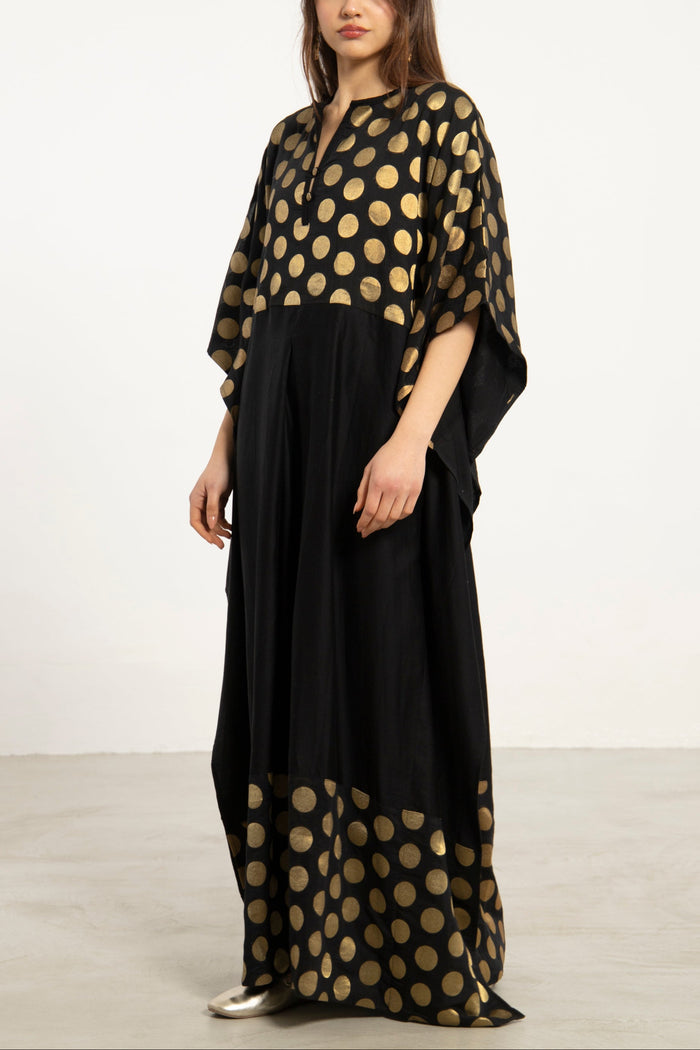Woman wearing a black dress with gold polka dot patterns on a white background