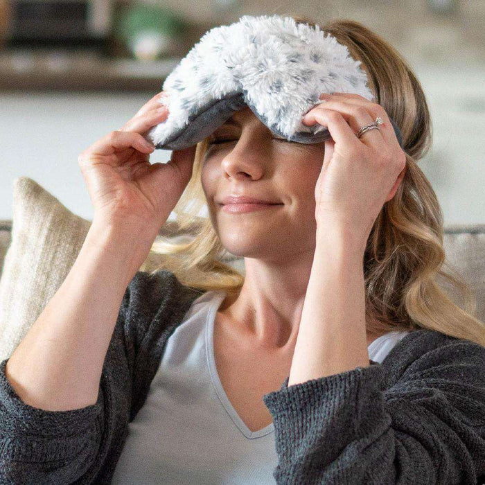 Woman wearing Snowy Warmies Eye Mask: Microwavable bliss for serene relaxation.