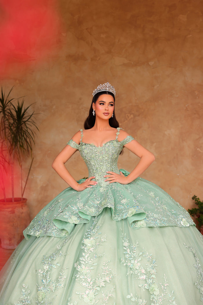 A woman in a mint green ballgown with a tiara stands confidently in an elegant, floral-embroidered quinceañera dress.