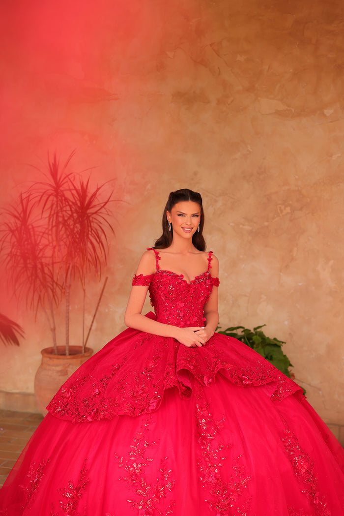 A woman in a vibrant red quinceañera ball gown poses with a warm-toned textured background and plants.
