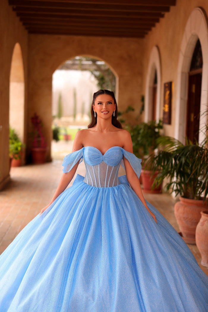 A woman wears a sparkling blue off-shoulder ball gown in an arched hallway with terracotta pots.