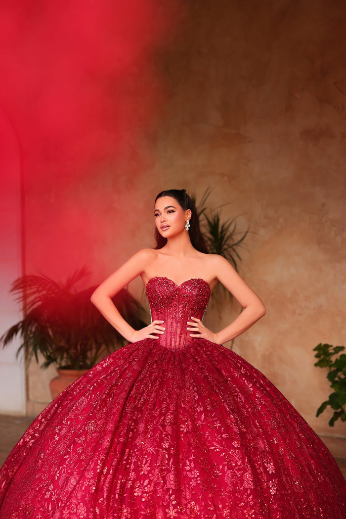 A woman in a vibrant red sparkling ball gown poses confidently against a warm-toned background.