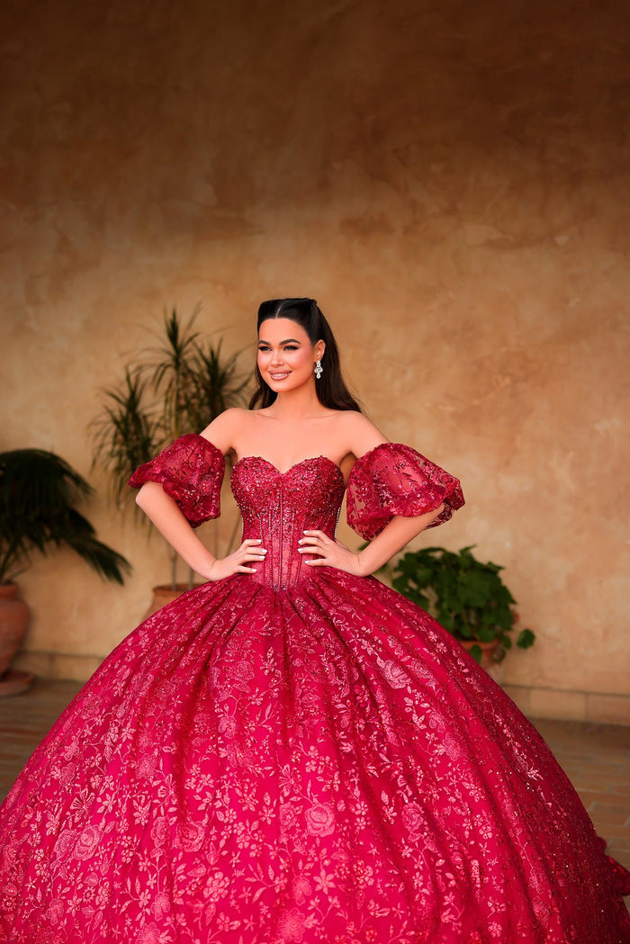 A woman in a vibrant red ball gown with sequined fabric and puffy sleeves poses elegantly against a warm background.