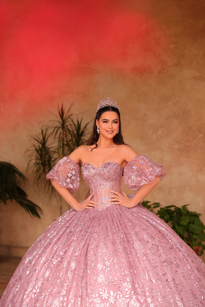 A woman in a sparkling pink ball gown and tiara poses with confidence against a warm-toned background.