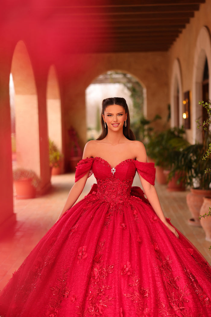 A woman in a vibrant red ball gown stands in an arched corridor with terracotta walls.