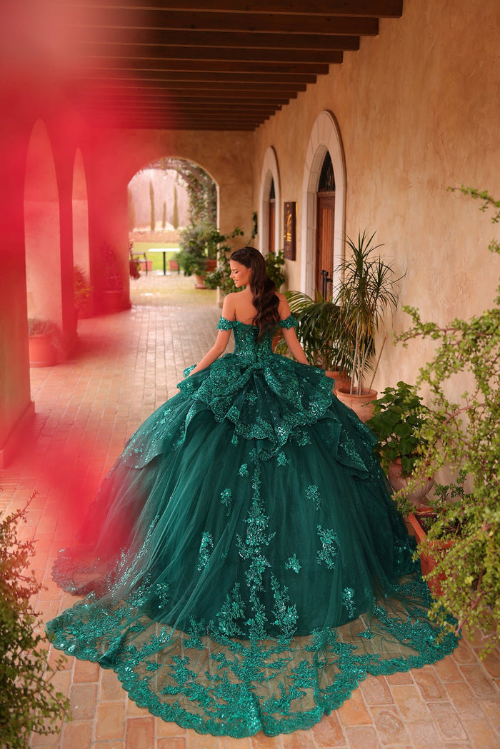 A woman wears an emerald green ballgown with intricate lace, standing in an arched courtyard with plants.