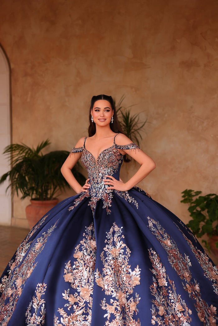 A woman in a navy blue ball gown with intricate floral embroidery poses confidently against a warm background.