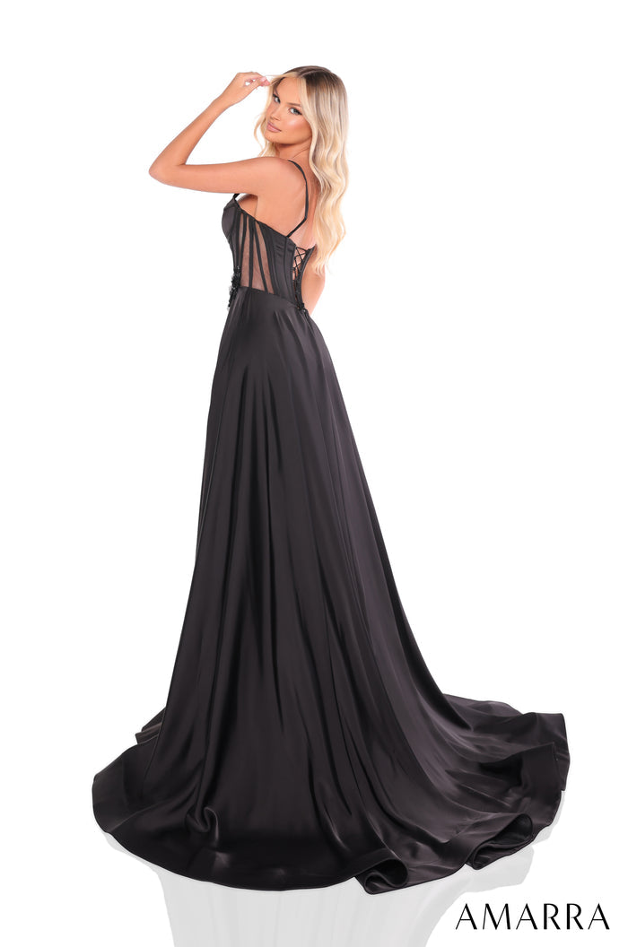 A blonde woman in a black satin corset gown with a flowing train poses elegantly against a white background.