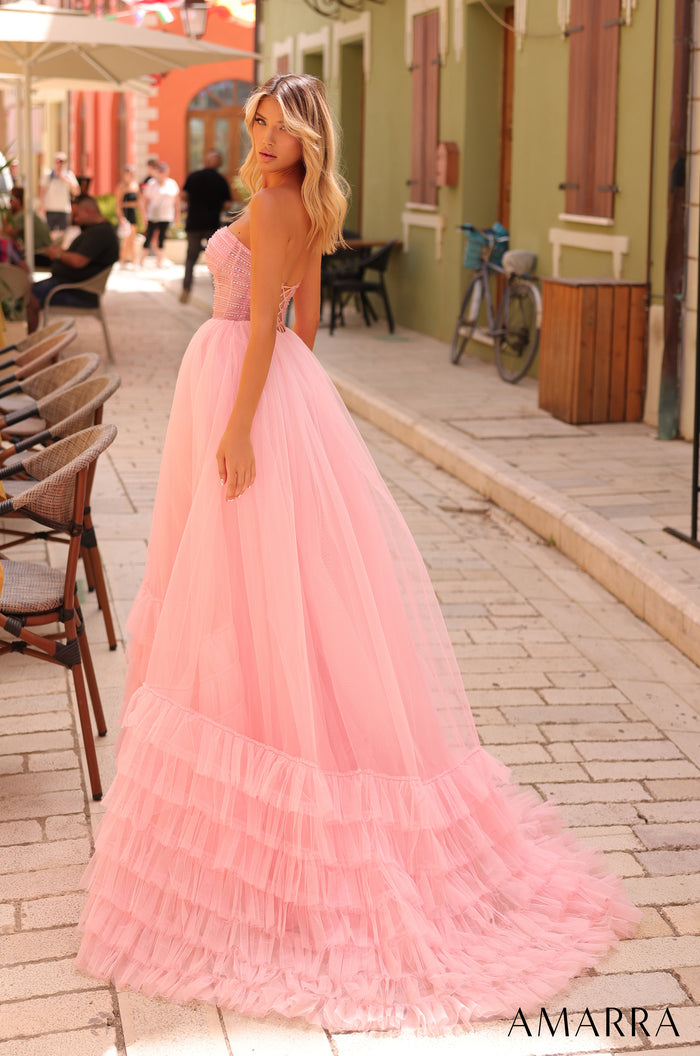 A woman wears a voluminous pink tulle gown with a strapless bodice, standing on a charming cobblestone street.