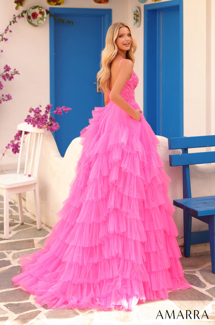 Blonde woman in a pink tiered tulle ball gown poses in a Mediterranean-style setting with blue doors.