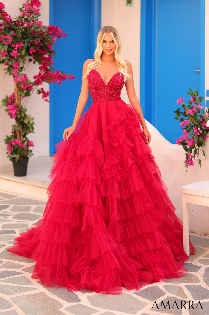 A flowing red ball gown with a sequined bodice and tiered tulle skirt, styled against a blue door with pink flowers.