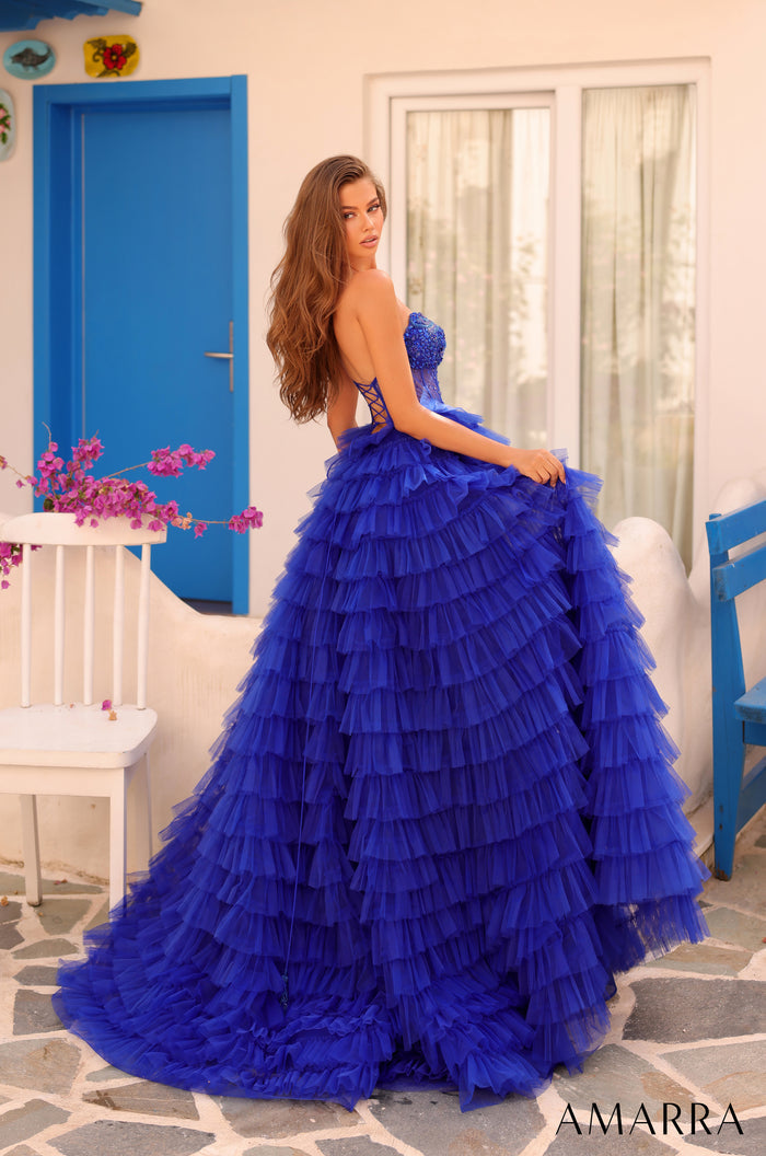 A model wears a royal blue tiered tulle ball gown with a corset top in a Mediterranean-style setting.