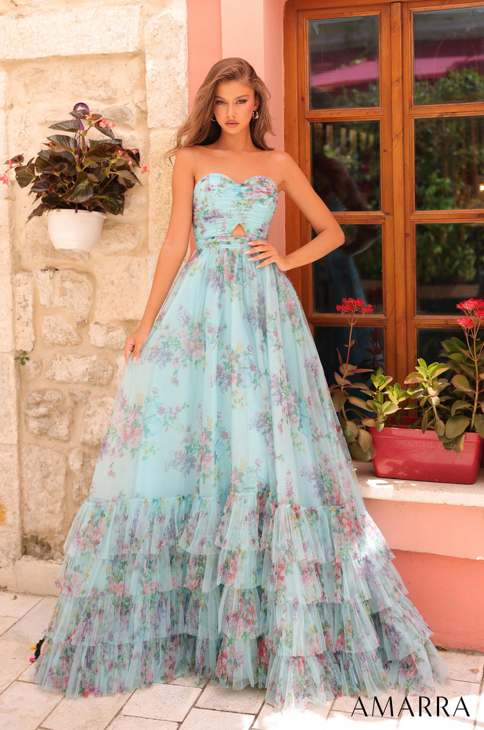 A strapless Light Blue/Multi floral tulle ballgown with tiered skirt, posed against a stone wall and wooden window.