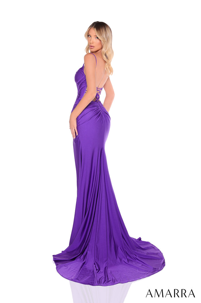 A model wears a long purple backless mermaid gown with a dramatic train, posing sideways.