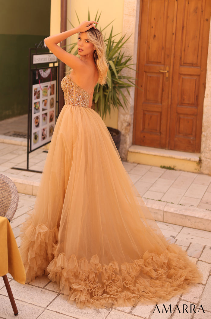 A golden tulle ball gown with a beaded bodice and ruffled skirt, photographed outdoors near a wooden door.