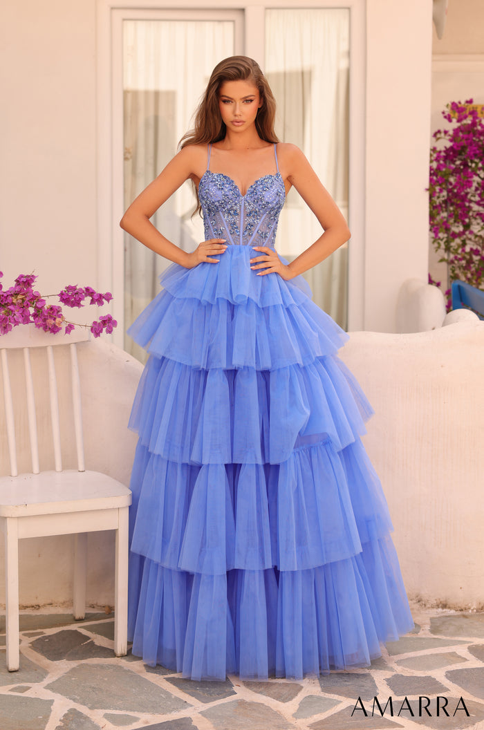 A tiered periwinkle tulle ball gown with a beaded corset bodice, styled on a model near flowering plants.