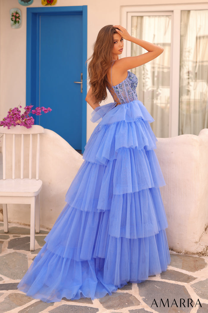 A model wears a blue tiered tulle ball gown with a beaded corset bodice against a blue door backdrop.