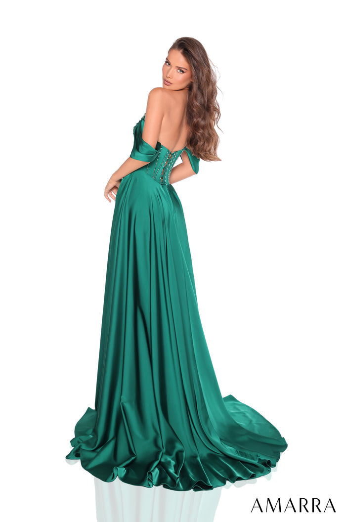 A woman wears an emerald green off-shoulder satin gown with a corset-style bodice and flowing train.