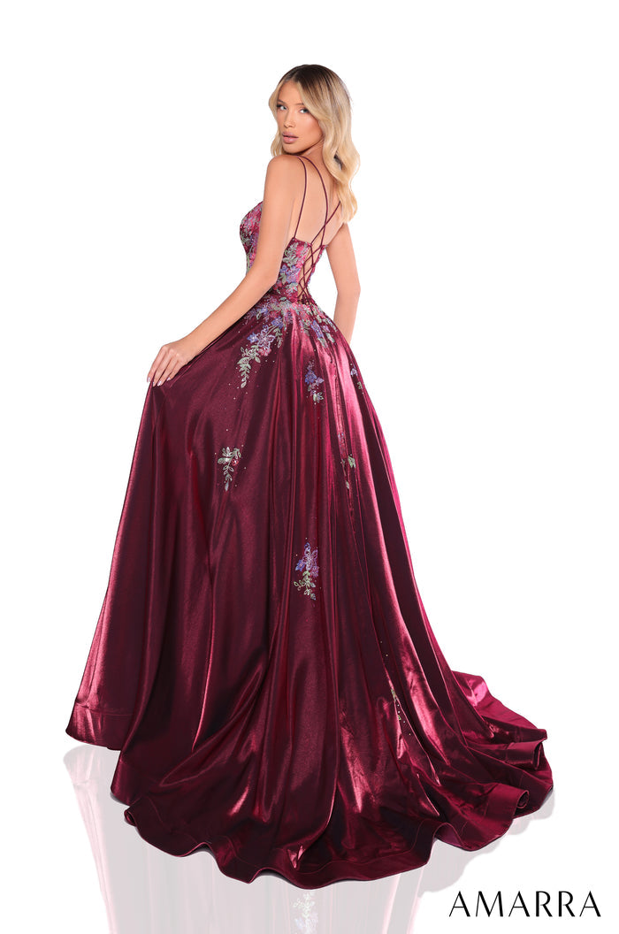 A person wears a burgundy velvet ball gown with floral embellishments and criss-cross back straps.