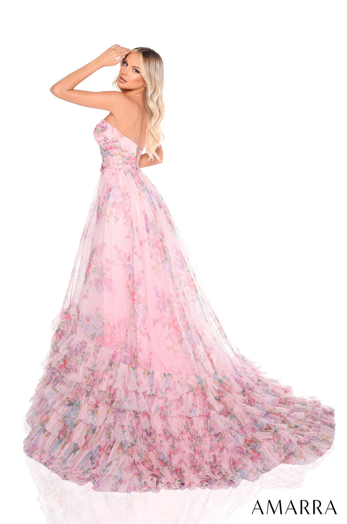 A blonde woman in a pink floral tulle ball gown poses elegantly against a white background.