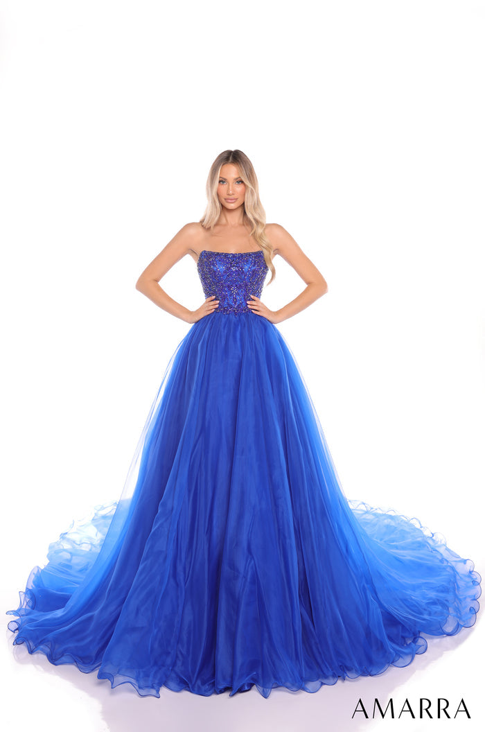 A model wears a strapless, sequined Royal Blue ball gown with a full, flowing tulle skirt.