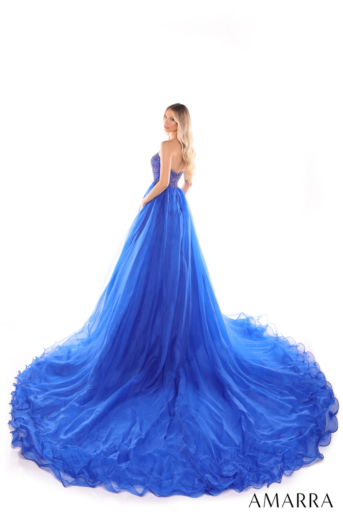 A woman wears a voluminous royal blue ballgown with a sweetheart bodice and dramatic ruffled train.