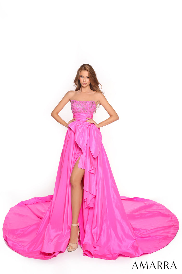 A model wears a strapless fuchsia gown with embellished bodice, high slit, and dramatic flowing skirt.