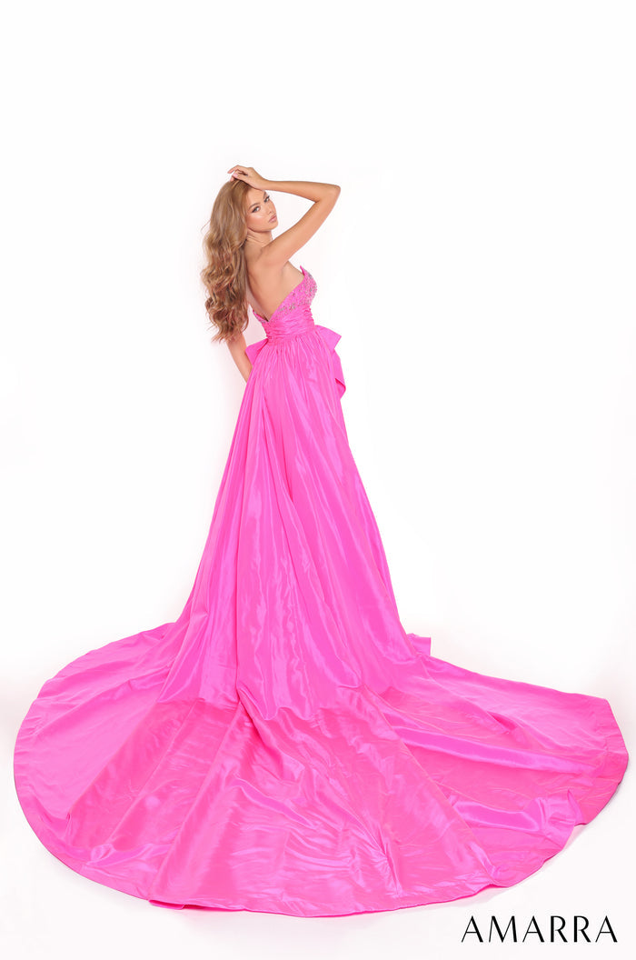 A woman in a flowing bright pink one-shoulder gown poses dramatically with a long, sweeping train.