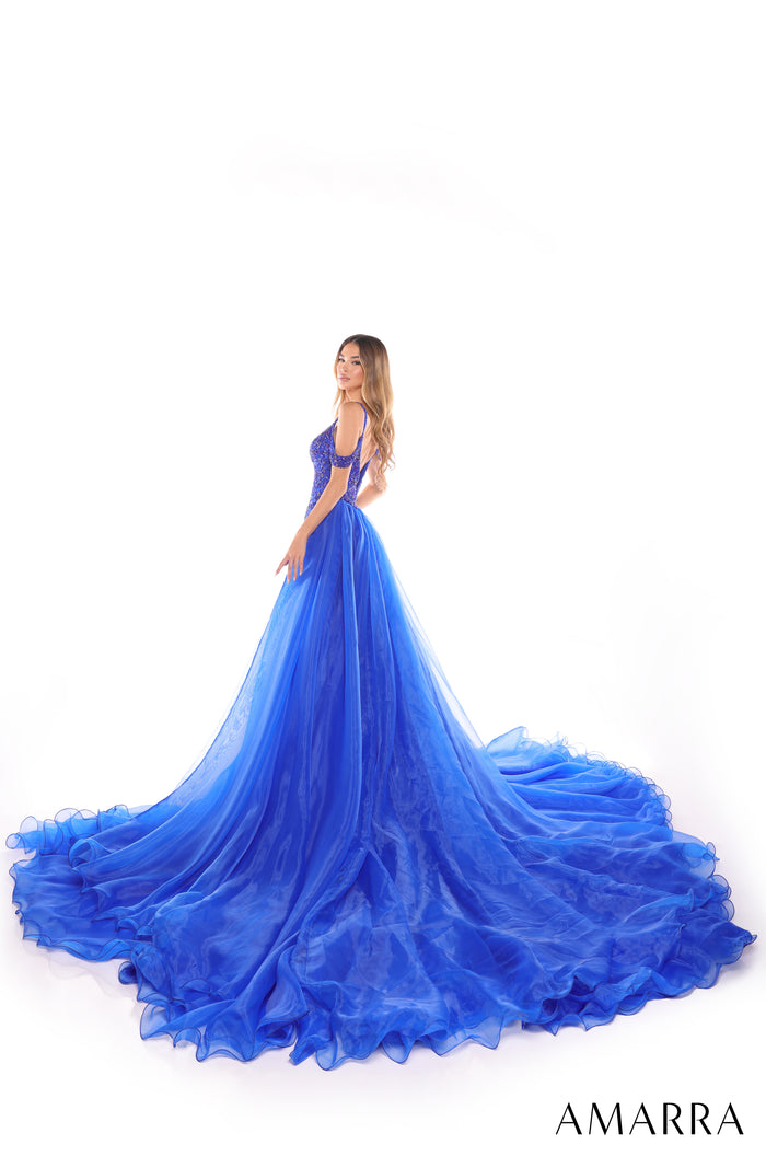 A woman wears a voluminous royal blue ball gown with a beaded bodice and sweeping ruffled train.